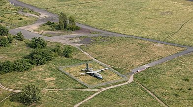 Luftbild eines umzäunten Flugzeugs auf einer Rasenfläche des Tempelhofer Felds