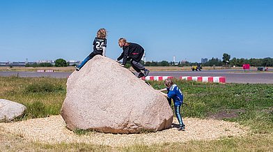 Kinder klettern auf einen großen Findling auf dem Tempelhofer Feld